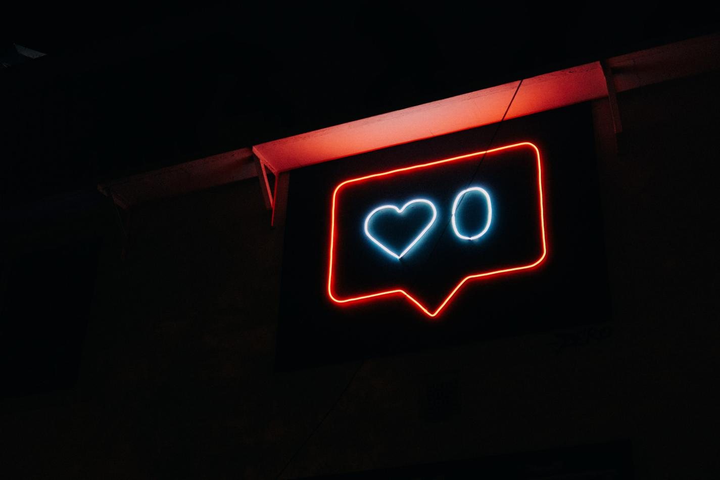 A neon sign in the dark that resembles an Instagram notification showing 0 likes.