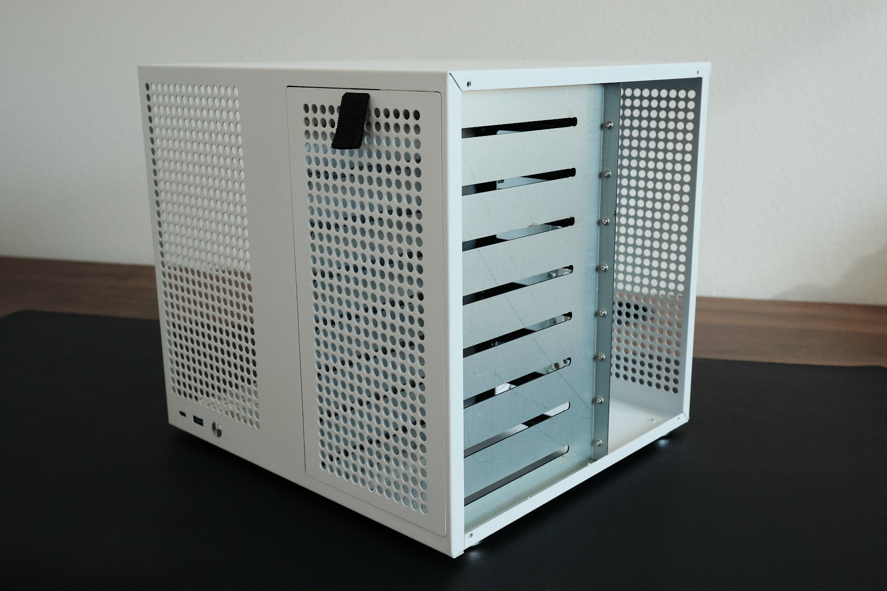 Front-left angle of the Sagittarius NAS case with both side panels removed, showing the drive bay cage and perforated ventilation panels