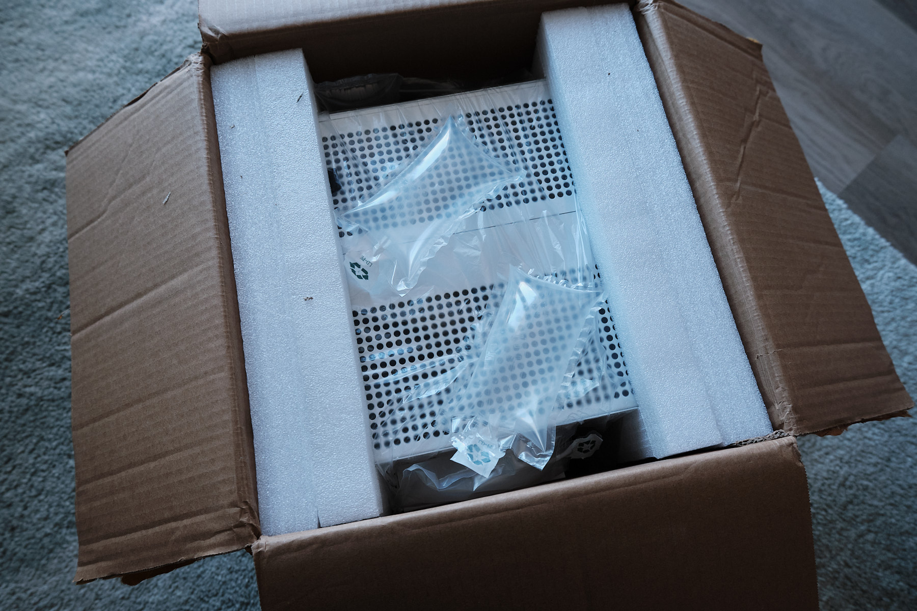 Top-down view into the shipping box showing the Sagittarius NAS case wrapped in plastic and sandwiched between two styrofoam pieces
